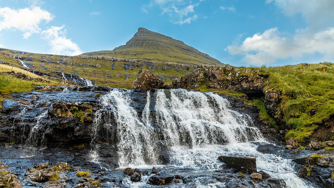 Europa, Färöer. Blick auf den Wasserfall, der einen Hügel auf den Färöer-Inseln hinunterstürzt.
