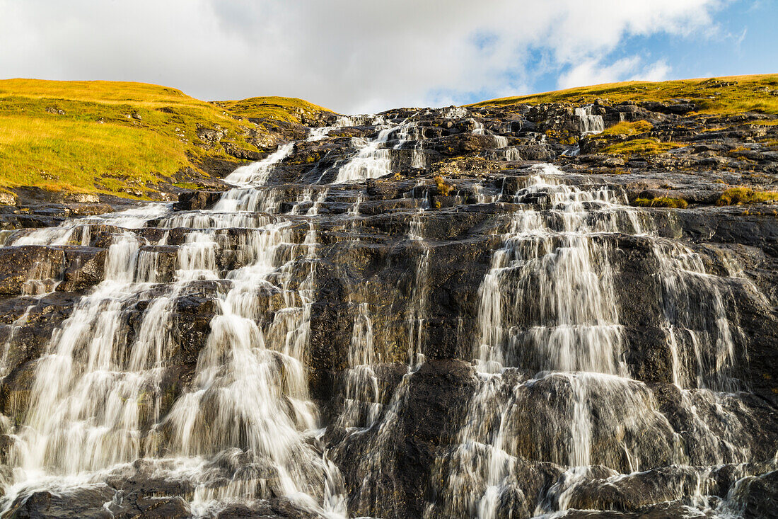 Europe, Faroe Islands. View of waterfall cascading down a hillside in the Faroe Islands.