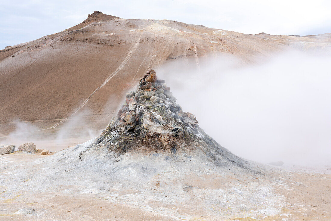 Island, Lake Myvatn District, Hverir Geothermalgebiet. Zahlreiche Thermalquellen sitzen neben einem Hügel aus rötlicher Lava.