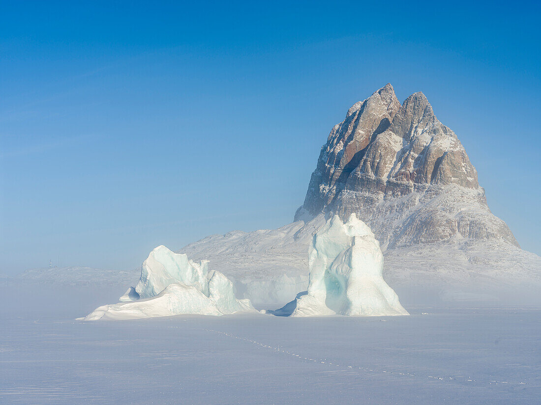Icebergs frozen into the sea ice of the Uummannaq Fjord System during winter. Background is Uummannaq. Greenland, Denmark.