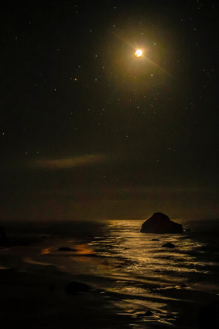 USA, Oregon, Bandon Beach. Lunar eclipse reflects on ocean shore at night.