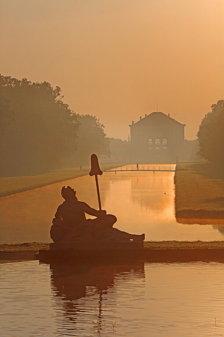 Sunrise in Nymphenburger Park with decorative figures of the cascade in the front and the Nymphenburg Palace in the back, Munich, Upper Bavaria, Bavaria, Germany