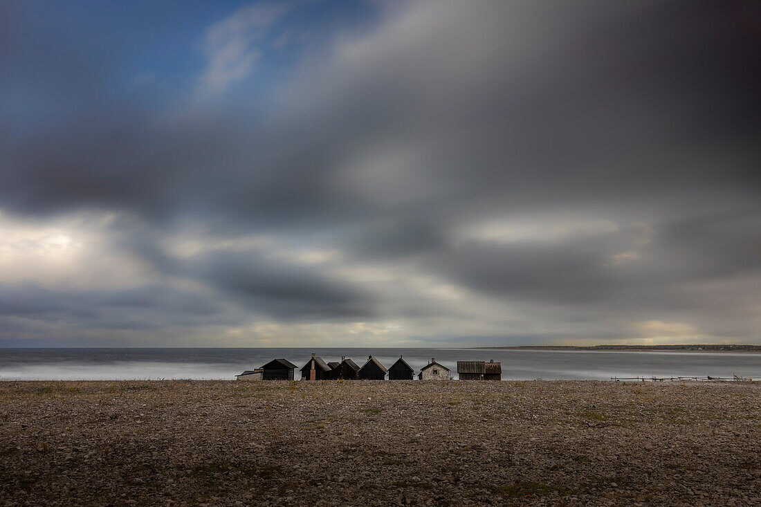 A row of lonely fisherman's huts stand on the stone beach. Menacing clouds in the sky. Helgumannen fiskelage. Faroe, Gotland County, Sweden.