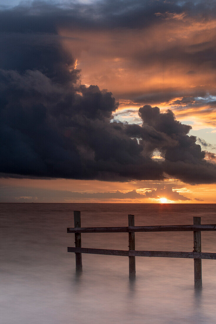 Sunset at the sea. wooden fence in the water. The sun peeks out from behind the clouds. Lolland, Denmark, Fehmarn Belt