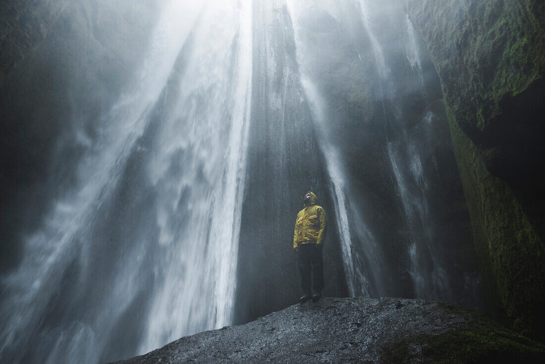 Mann mit gelbem Regenmantel am Wasserfall Seljalandsfoss in Island
