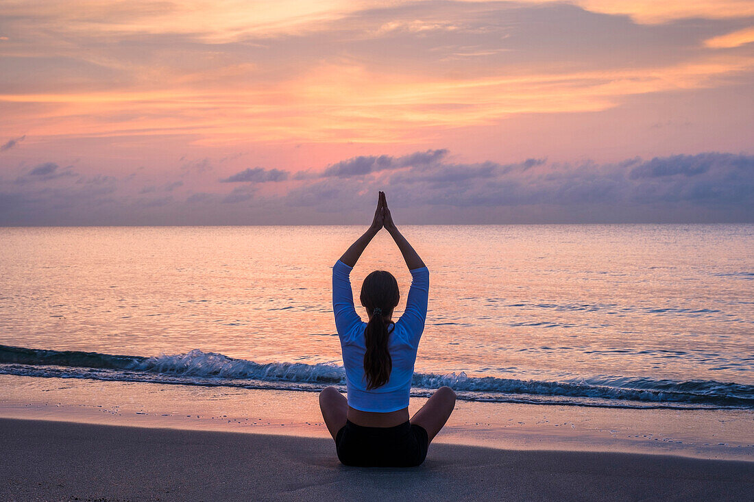 Frau praktiziert Yoga am Strand bei Sonnenuntergang