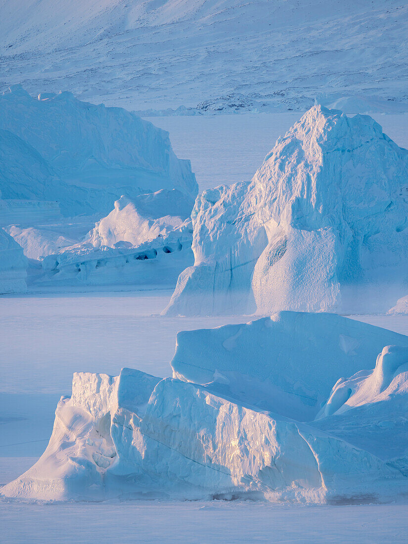 Icebergs frozen into the sea ice of the Uummannaq Fjord System during winter. Background is Nuussuaq Peninsula, Greenland, Denmark.