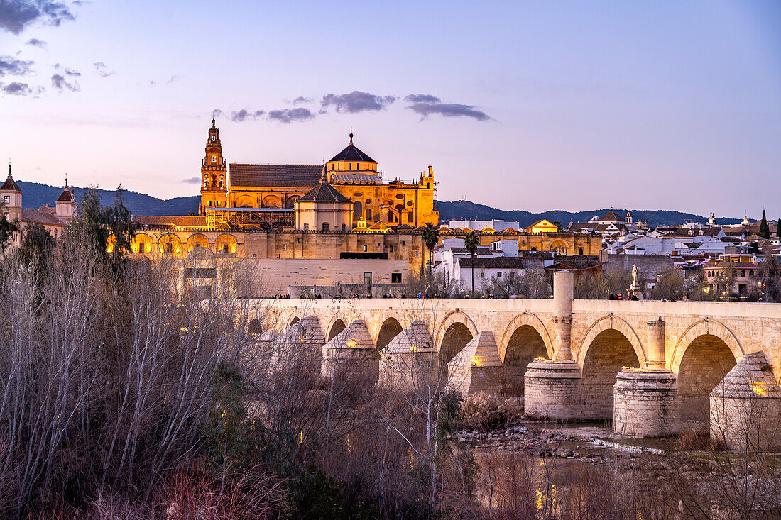 Römische Brücke über den Fluss Río Guadalquivir und die Mezquita - Catedral de Córdoba in der Abenddämmerung, Cordoba, Andalusien, Spanien 