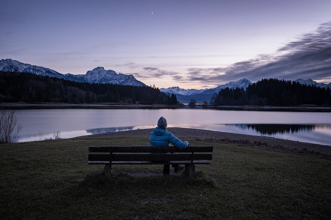 Bench with woman with a view over the Forggensee to the Tegelberg, Säuling and Tannheim mountains, Allgäu, Bavaria, Germany, Europe