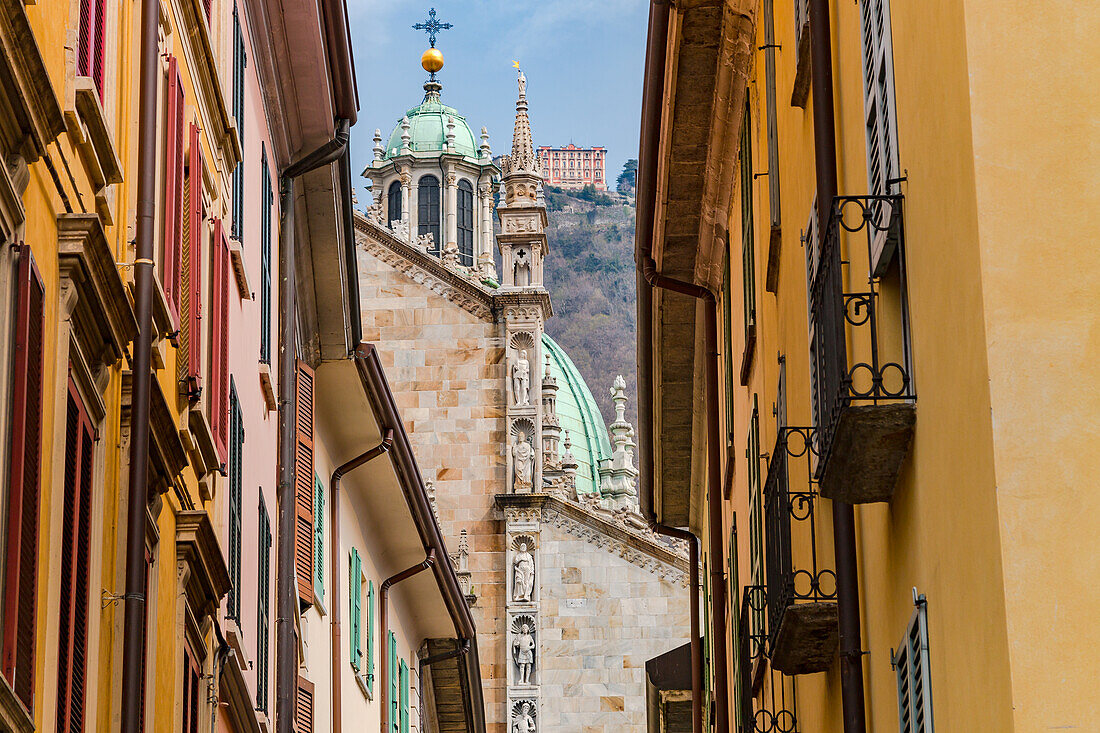 View along the narrow streets of Como's old town towards the Duomo and surrounding mountains, Lake Como, Italy