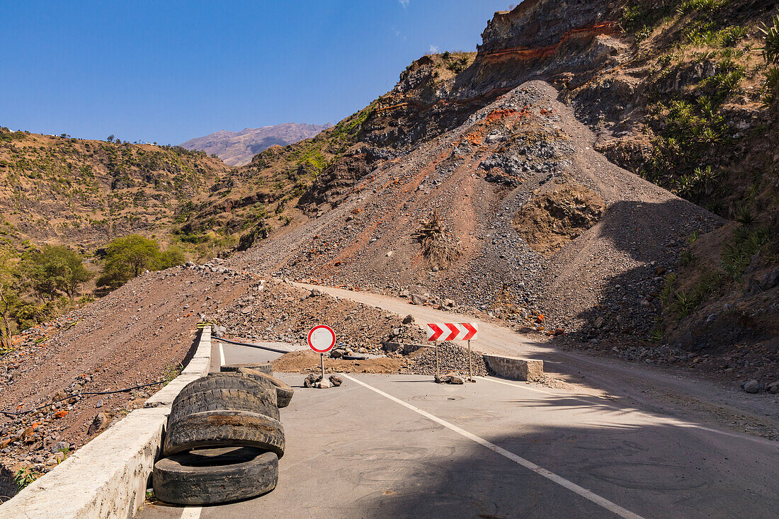 Eine geteerte Straße endet abrupt mit einem Schild da ein Erdrutsch mit Lavagestein den Weg blockiert, Insel Fogo, Kapverden