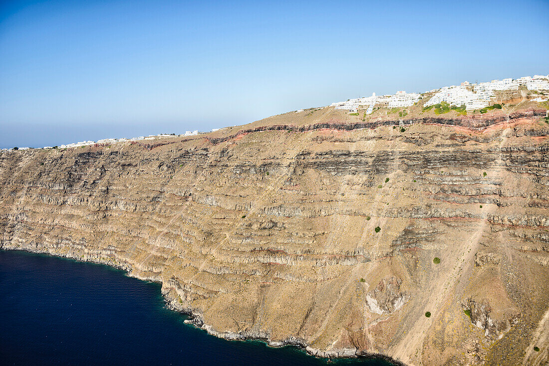 Die Klippen und Felsformationen einer Insel in der Ägäis, mit einer Stadt aus weiß getünchten Häusern auf der Spitze der Klippen.