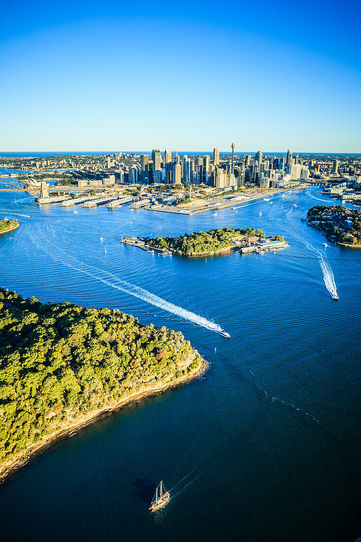 Aerial view over the city of Sydney, the water channels and the coastline of islands and boat traffic.
