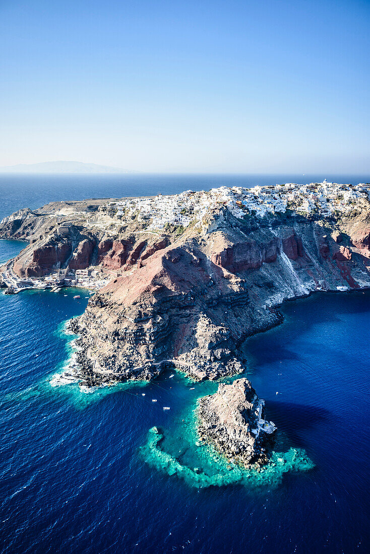 Luftaufnahme einer Insel im tiefblauen Meer der Ägäis, Felsformationen, weiß getünchte Häuser, die auf den Klippen thronen.