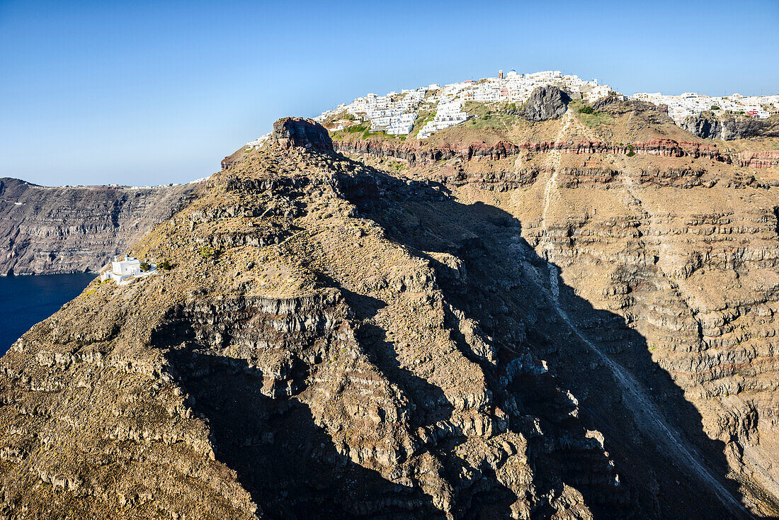 Luftaufnahme einer Stadt an der Spitze einer steilen Klippe auf der Insel Egeo und dem gewundenen Pfad zu einem Haus unten an den steilen Hängen.