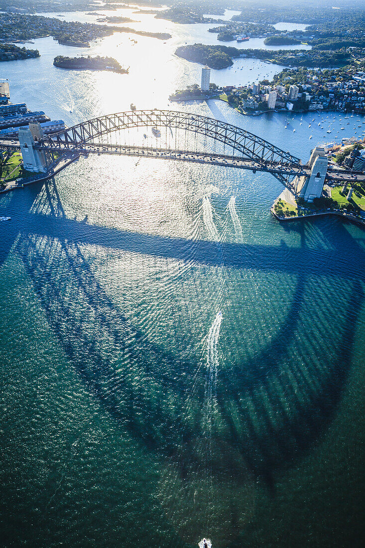 Die Sydney Harbour Bridge, der Schatten des Bogens auf dem Wasser und die Luftaufnahme der Landschaft.