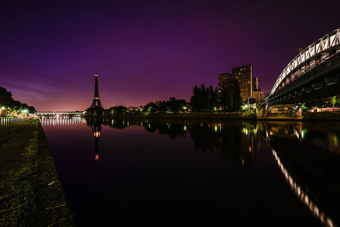 Ein Blick auf das Wasser der Seine bei Nacht, hohe Gebäude am Flussufer, der Eiffelturm in der Ferne.