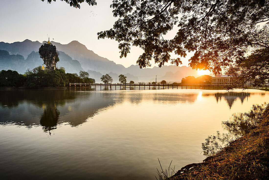 Sunrise over the lake at Hpa An, a footbridge, shrine and mountain landscape.
