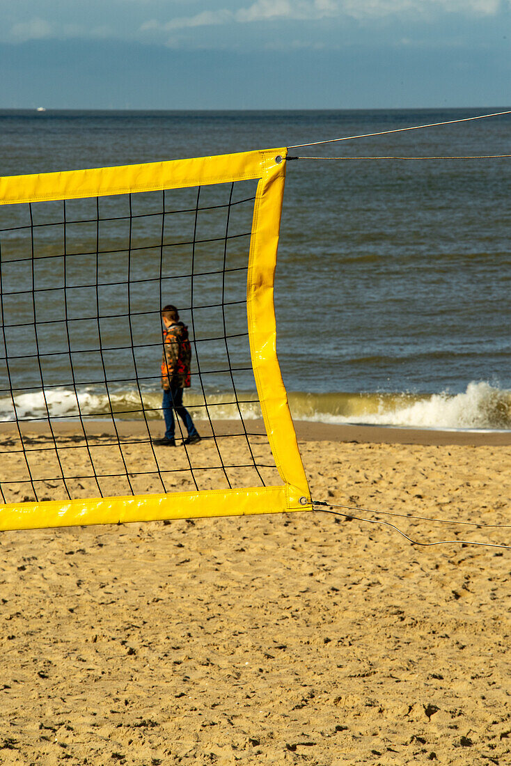 Kid on dutch beach walking behind a volleyball net.