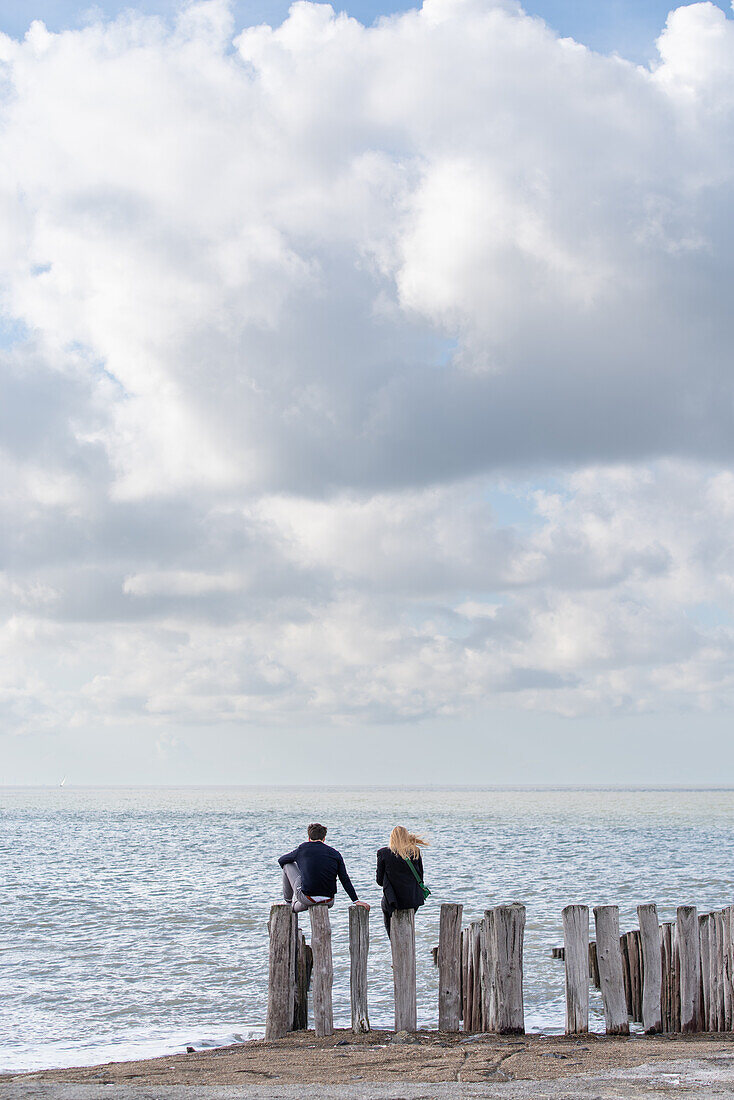 Ein Paar sitzt auf Wellenbrecher, Strand von Groede in der Provinz Zeeland, Niederlande.