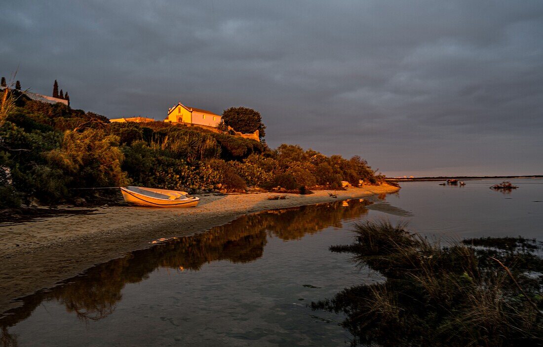 Rowing boat on the beach and church of the heritage village of Cacela Velha in the evening light, Algarve, Portugal