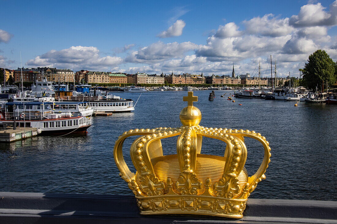 Golden crown on Skeppsholmen bridge with boats in harbor behind, Stockholm, Sweden, Europe