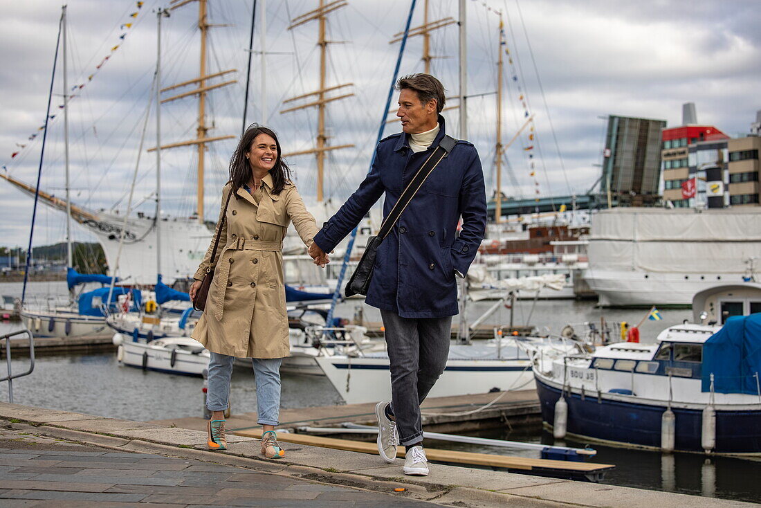 Couple walking along the water's edge at the marina, Gothenburg, Vaster-Gotaland, Sweden, Europe