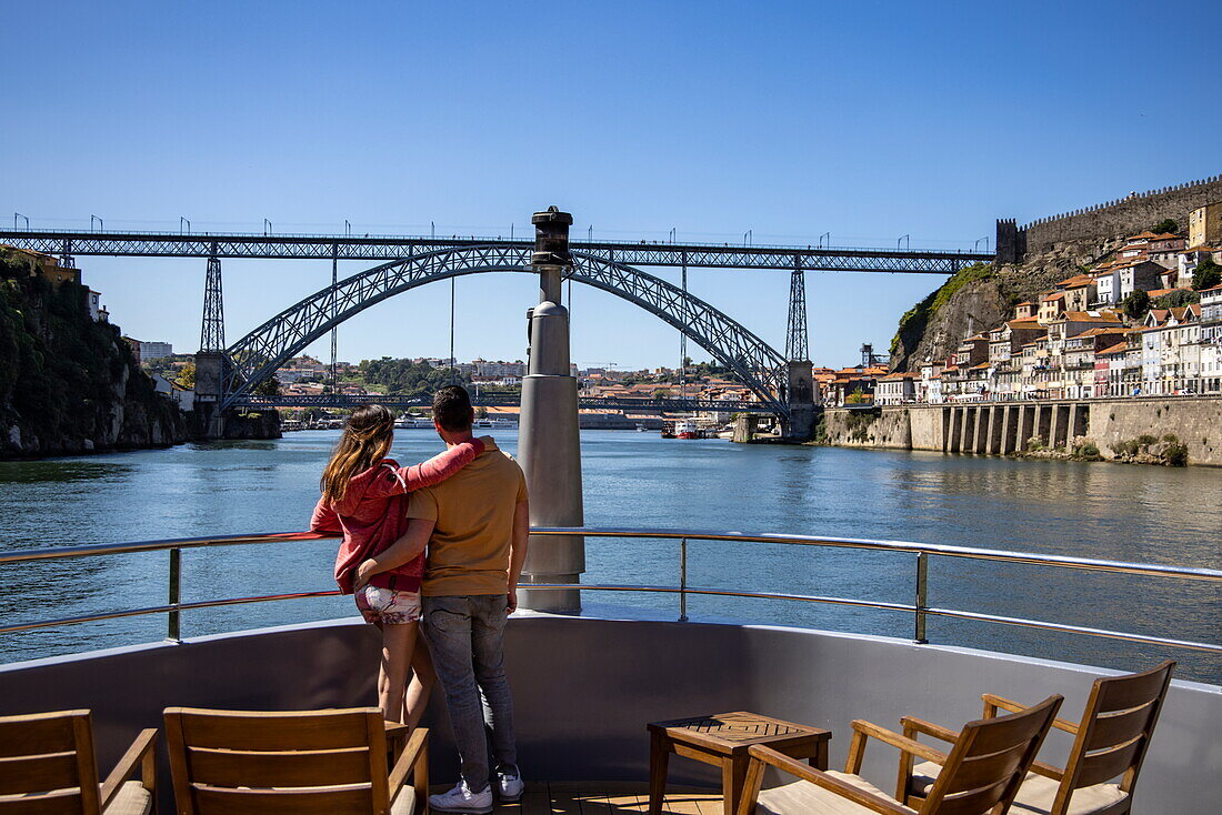 Couple on bow deck of river cruise ship Douro Serenity (Nicko Cruises) on Douro river with Ponte Dom Luis I bridge, Oporto, Oporto, Portugal, Europe