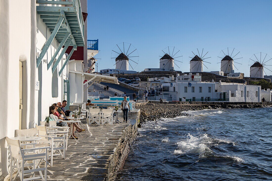 Tables and chairs in a Little Venice restaurant with the famous Mykonos windmills in the background, Mykonos, South Aegean, Greece, Europe