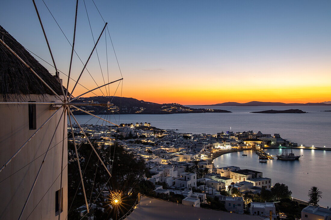 Windmill in front of the 180º Sunset Bar overlooking the town with the famous Mykonos windmills, harbor and islands at dusk, Mykonos, South Aegean, Greece, Europe