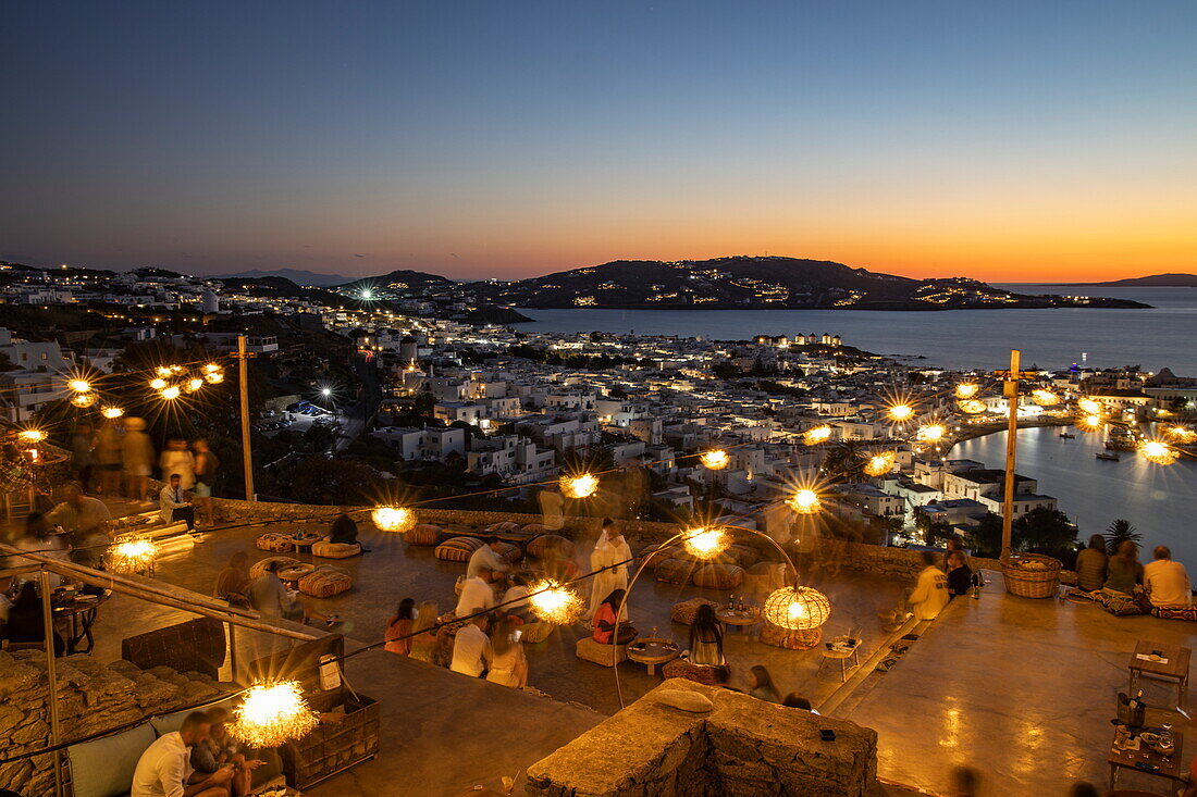 People chilling at the 180º Sunset Bar overlooking the town and islands at dusk, Mykonos, South Aegean, Greece, Europe