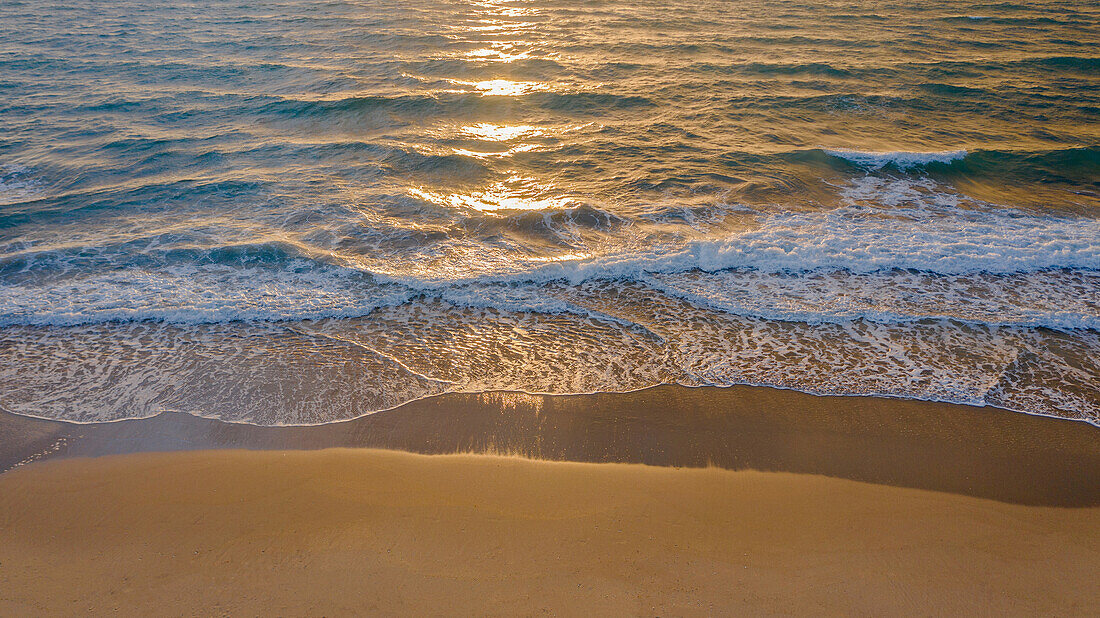 Ruhige Meereswellen, die bei Sonnenaufgang auf den Sandstrand rollen