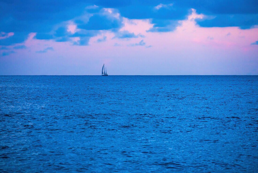 Ocean at sunrise with lone sailboat in distance