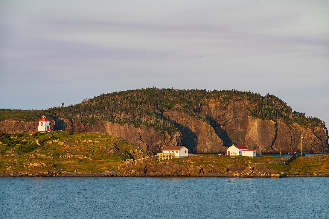 Canada, Labrador, Newfoundland, Trinity, Sea coastline with distant Fort Point Lighthouse at sunset