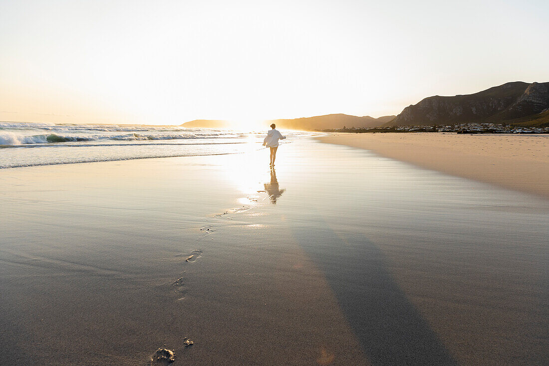 South Africa, Hermanus, Teenage girl (16-17) walking on Grotto Beach at sunset