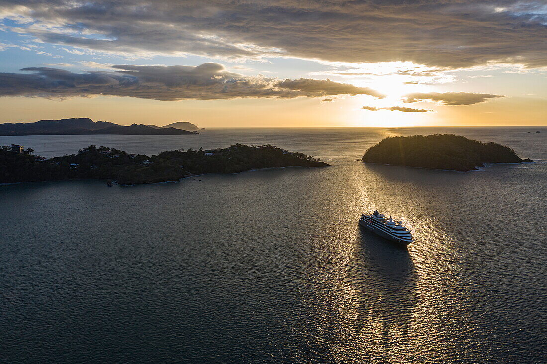 Luftaufnahme von Expeditionskreuzfahrtschiff World Voyager (nicko cruises), Silhouette bei Sonnenuntergang mit Landzunge und Insel dahinter, Playa Flamingo, Guanacaste, Costa Rica, Mittelamerika