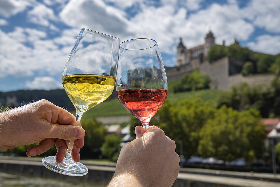 Anstoßende Weingläser am Mainufer mit Blick auf die Festung Marienberg, Würzburg, Franken, Bayern, Deutschland, Europa