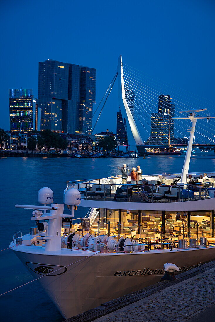 River cruise ship Excellence Countess (travel agency Mittelthurgau) with Erasmus Bridge (Erasmusbrug) over Nieuwe Maas and modern buildings at night, Rotterdam, South Holland, The Netherlands, Europe