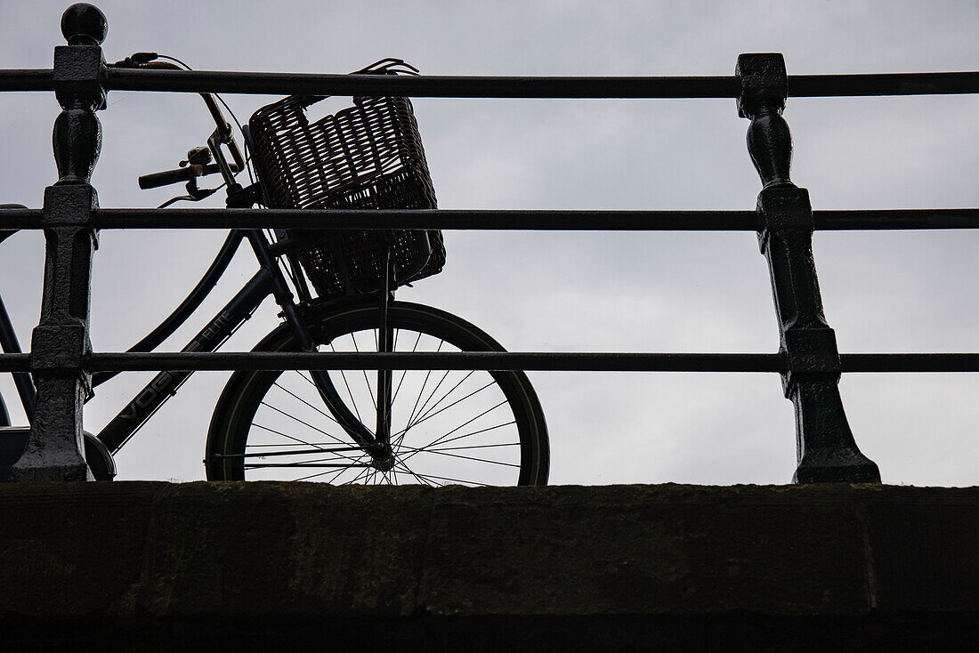 Silhouette eines Fahrrads mit Korb auf einer Brücke über Kanal, Amsterdam, Nordholland, Niederlande, Europa