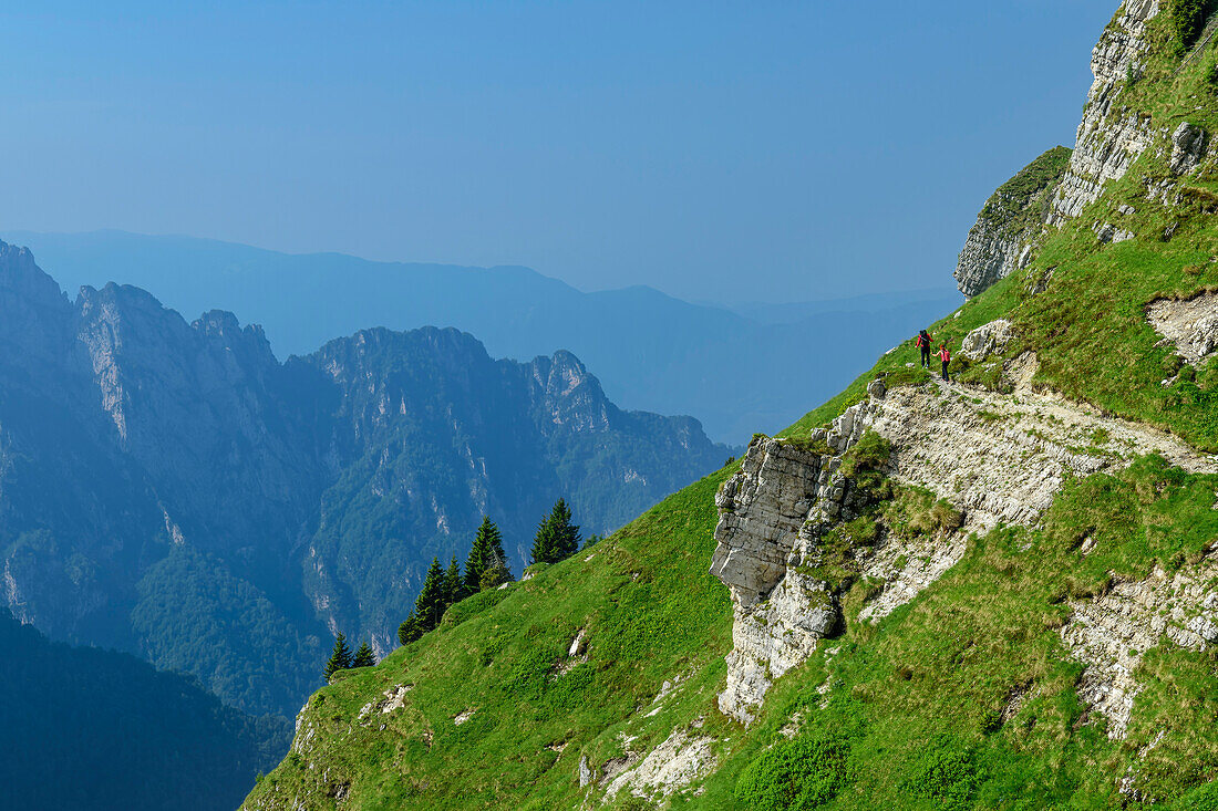 Two people hiking through steep grassy slopes, Feltriner Berge, Belluneser Höhenweg, Dolomites, Veneto, Venetia, Italy