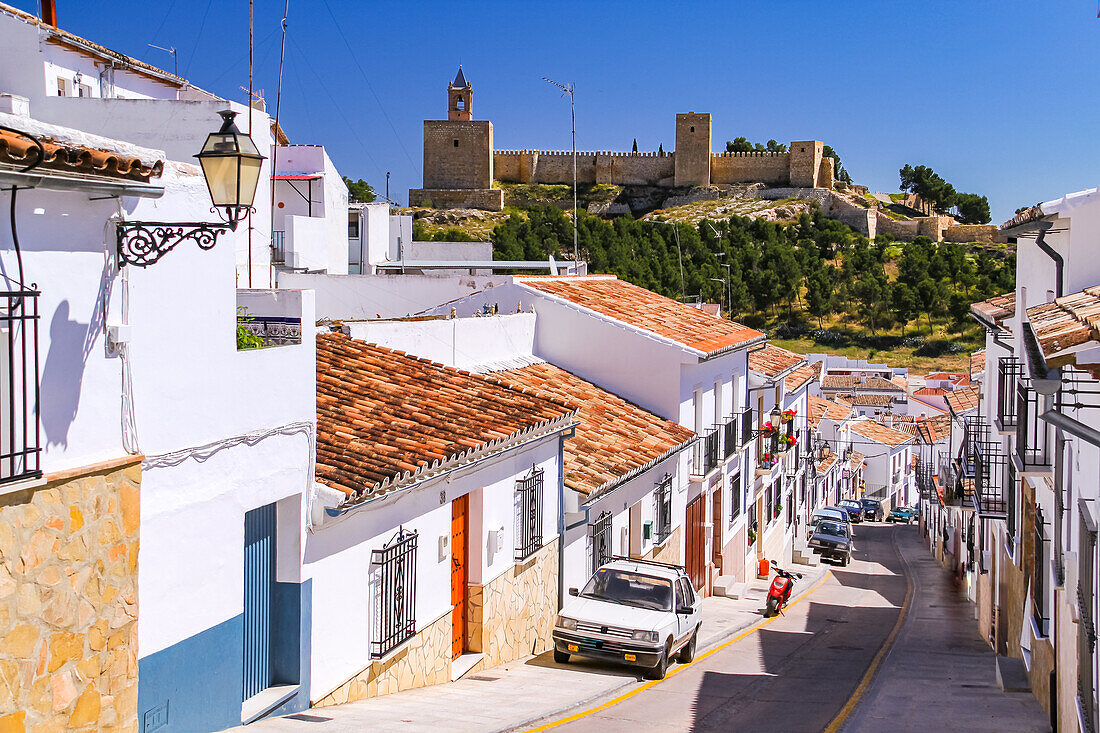 Blick entlang einer Straße in Antequera auf die Festung Alcazaba de Antequera oberhalb der Stadt in Andalusien, Spanien