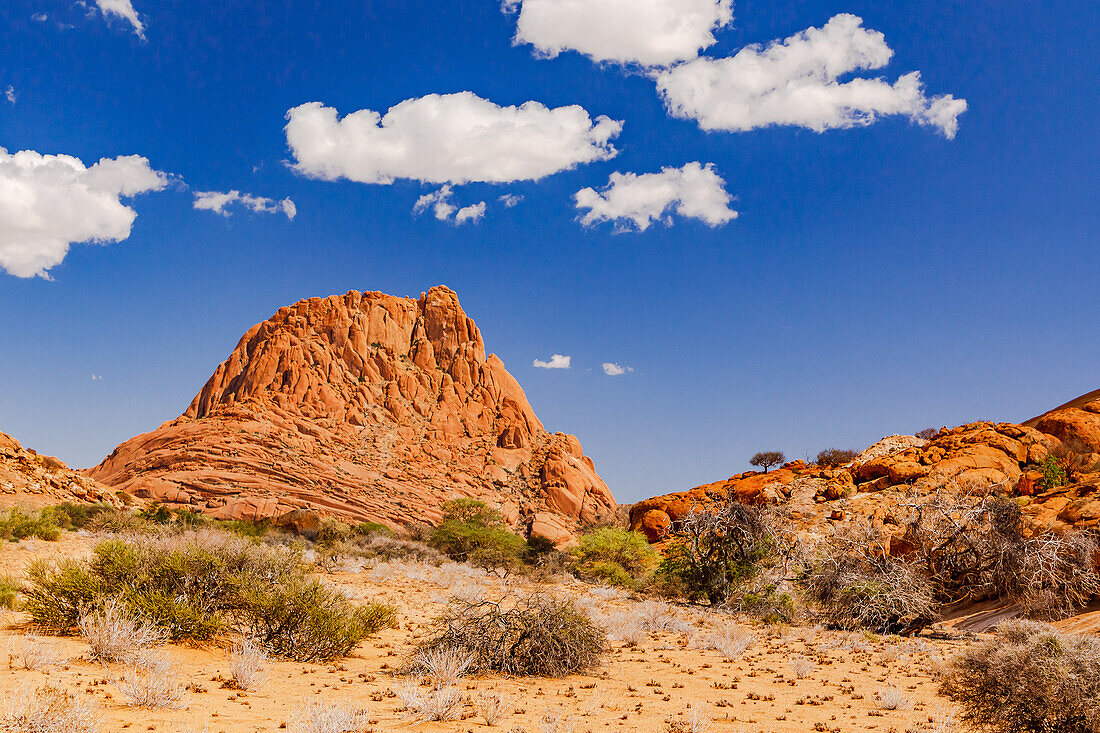 A monolith of the Spitzkoppe Inselberg Group in the savanna under a blue sky with fair weather clouds, Namibia, Africa