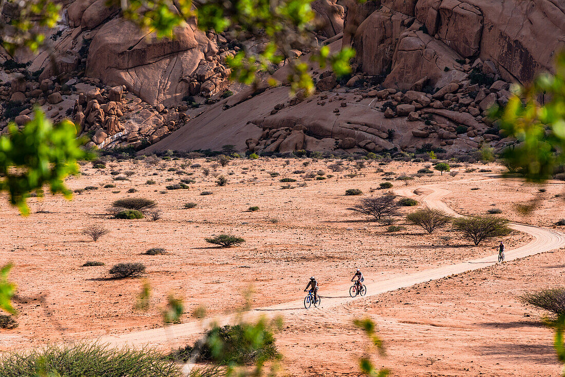 Several cyclists on a sandy path between the granite rocks of the Spitzkoppe Inselberg Group in Namibia, Africa