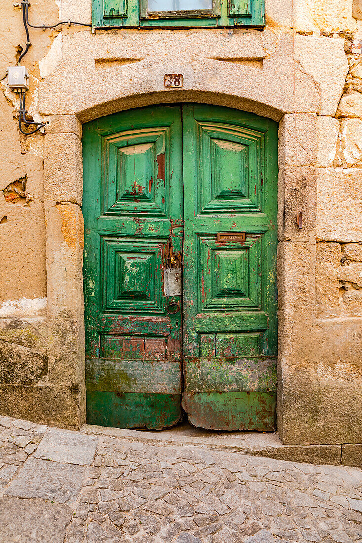 Verzierte grübe Doppeltüre aus Holz an der Steinfassade eines Hauses an einer Pflasterstraße in Lamego, Portugal