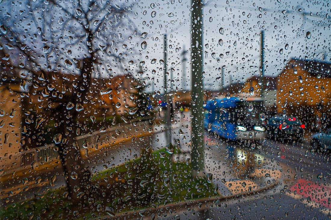 Regentropfen an einer Fensterscheibe mit Blick auf eine Kreuzung mit fahrenden Autos und einer Tram, Jena, Thüringen, Deutschland