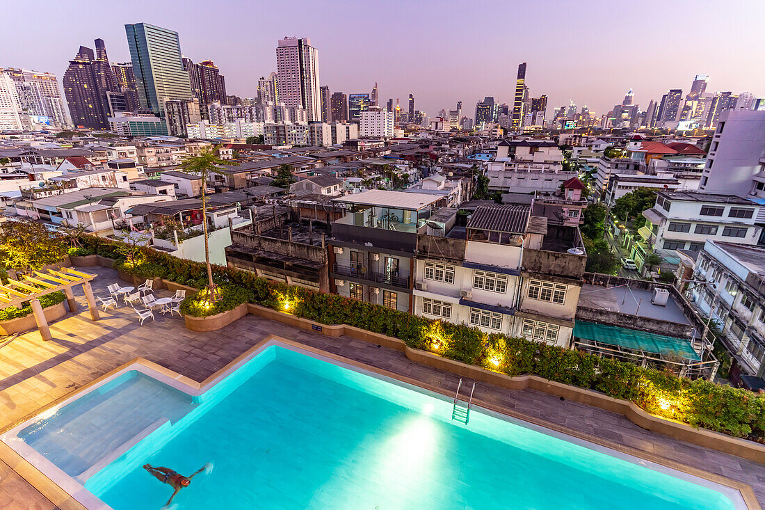 Illuminated swimming pool in front of Bangkok city view and skyline at dusk, Thailand, Asia