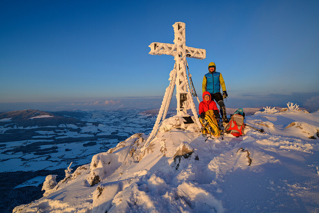 Man and woman winter hiking standing at the summit cross of the Schober, Schober, Salzkammergut, Salzkammergut Mountains, Salzburg, Austria