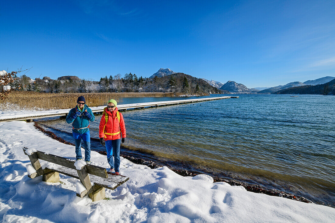 Man and woman hiking walking towards bench on the shore of Lake Fuschl, Fuschlsee, Salzkammergut, Salzkammergut Mountains, Salzburg, Austria