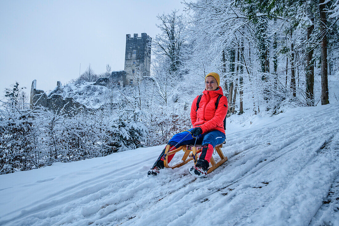 Woman sledding with the ruins of Falkenstein Castle in the background, Flintsbach am Inn, Inn Valley, Bavarian Alps, Upper Bavaria, Bavaria, Germany