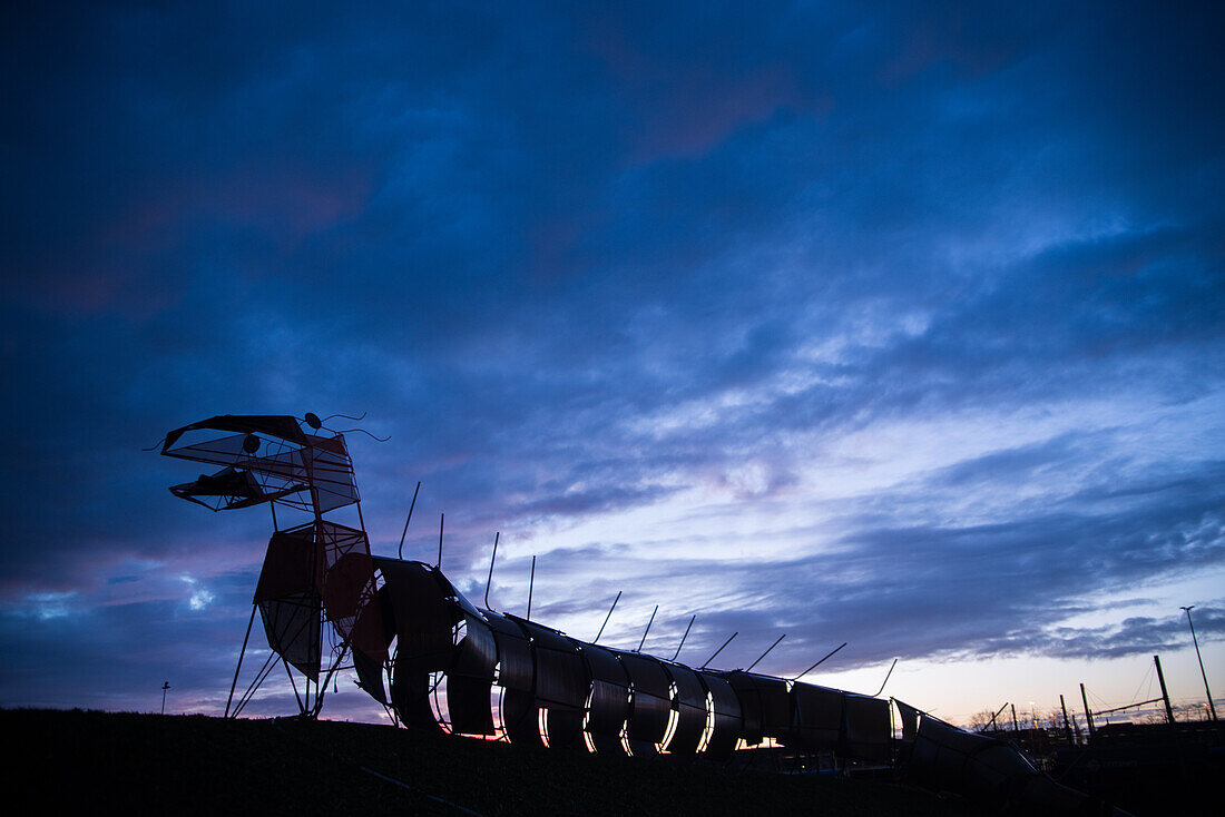 Metal sculpture of a dragon on a hill in the light of dusk.